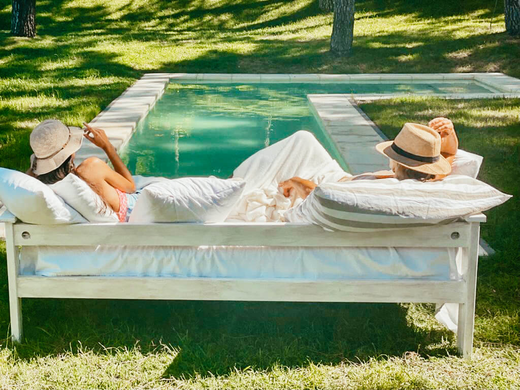 Dos huéspedes sentadas en un sillón al sol al borde de la pileta