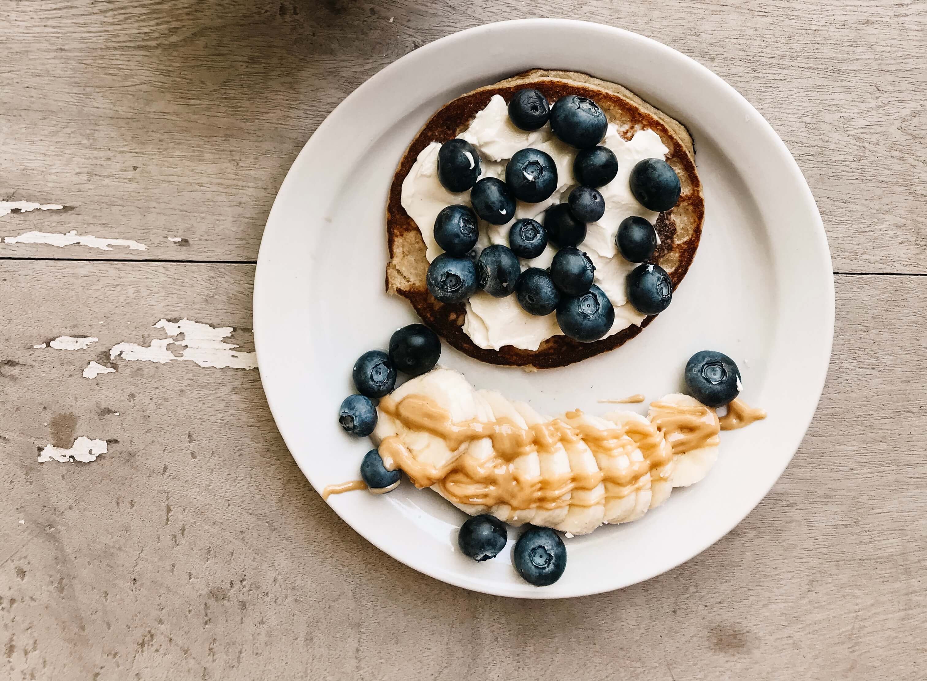 Desayuno de pancakes de banana con queso crema y arándanos acompañado de banana con mantequilla de maní