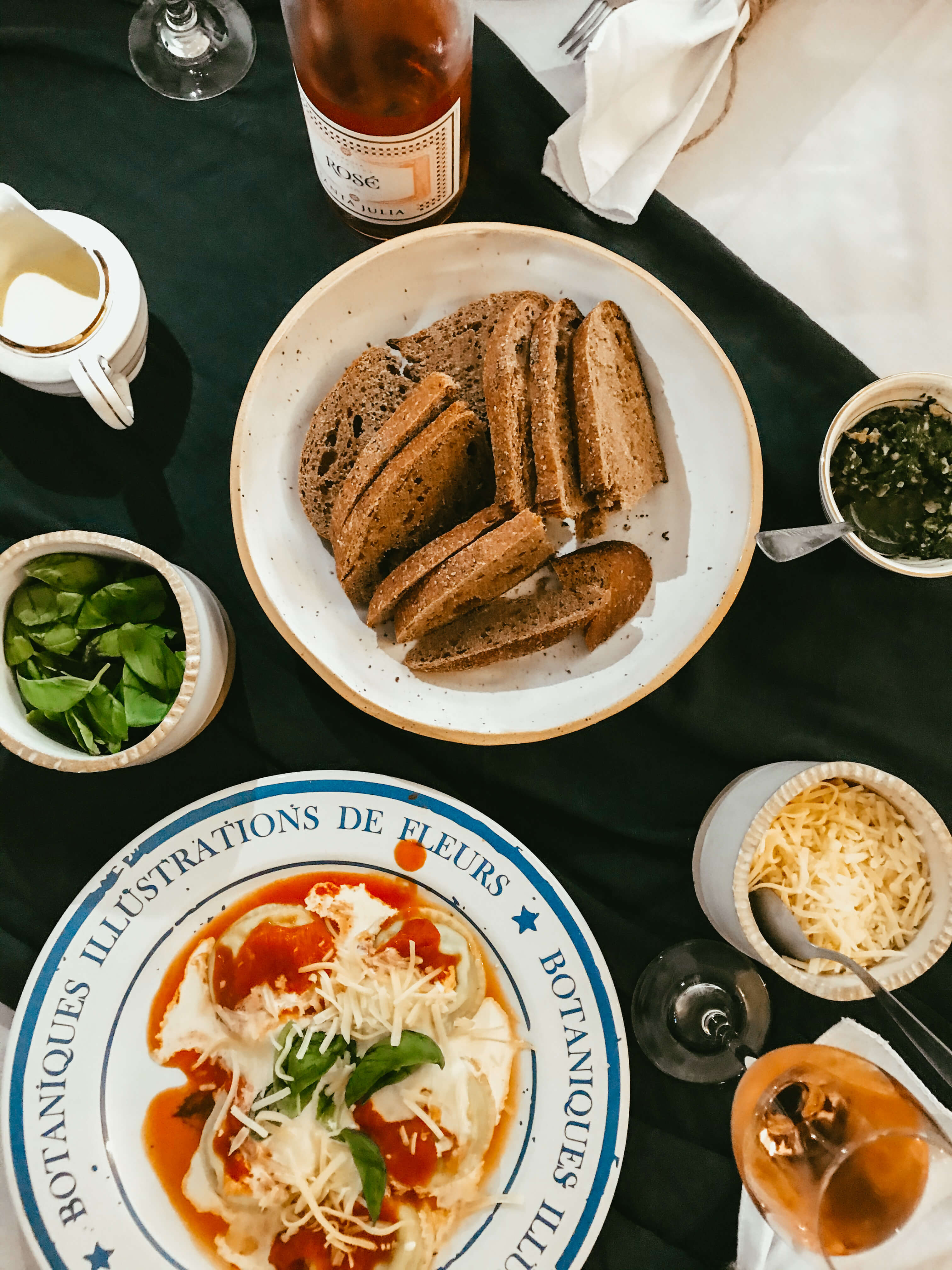 Almuerzo de comensales con sorrentinos, crema, vino rosado y pan de masa madre