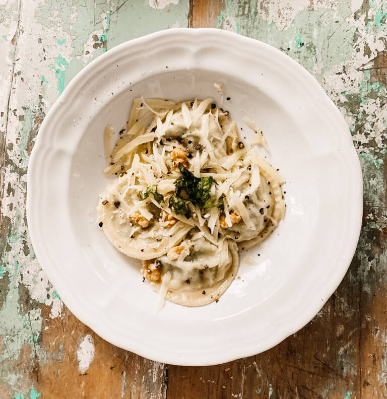 Plato de sorrentinos de espinaca y ricota con crema, queso rallado, nueces y albahaca